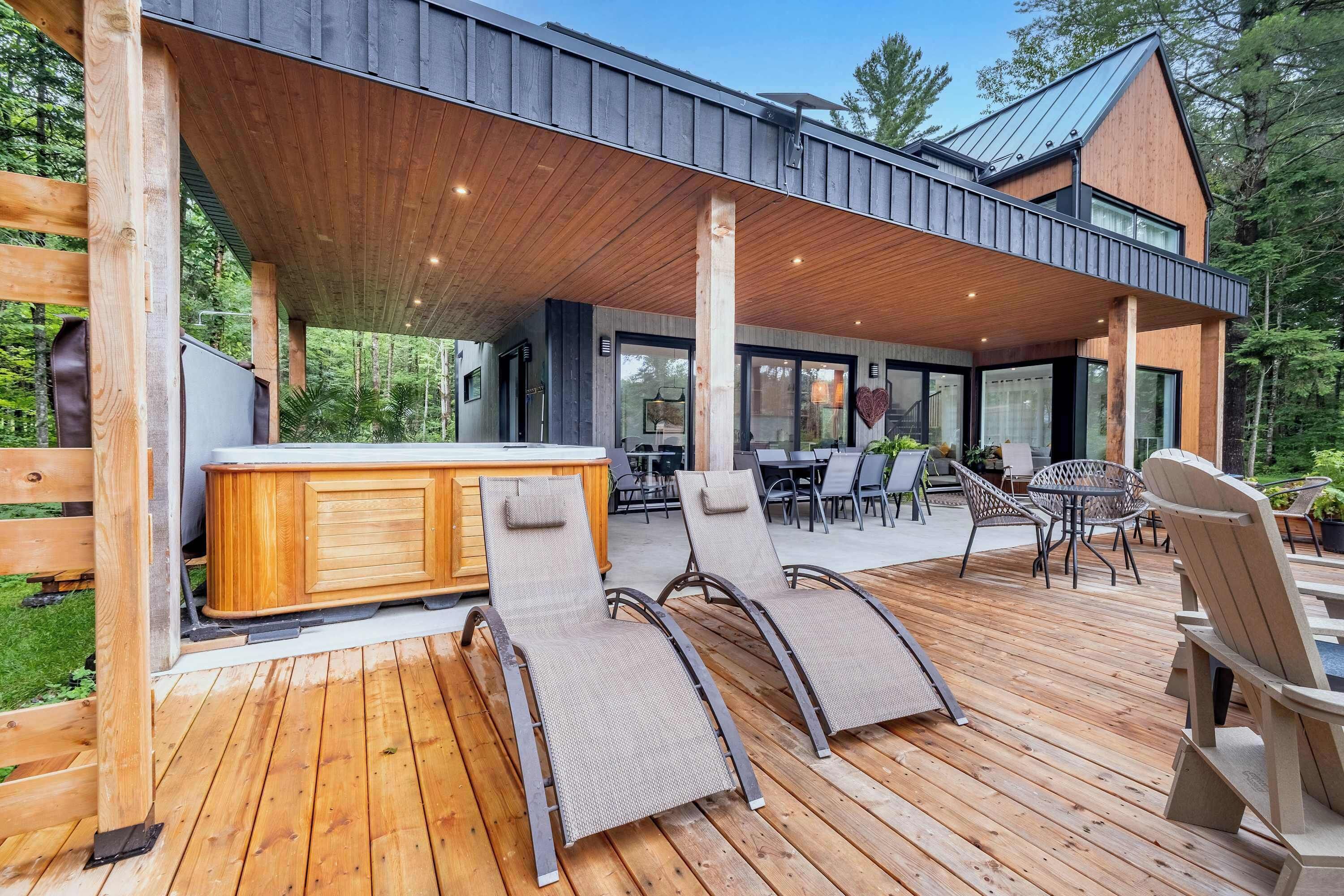 A covered outdoor deck with wooden flooring, lounge chairs, and a bar area.