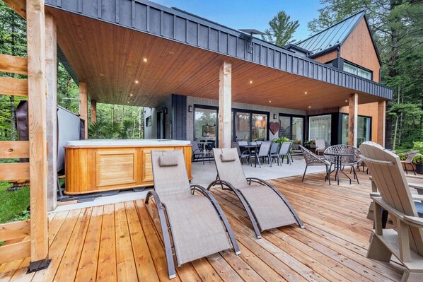 A covered outdoor deck with wooden flooring, lounge chairs, and a bar area.