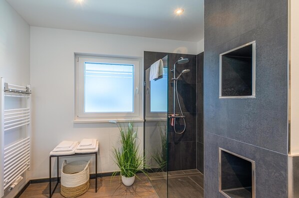 A modern bathroom with a glass shower enclosure, a white towel rack, a potted plant, and a window providing natural light. - "Sebastian" Vacation Rental in the Old Textile Factory in Malchow (Malchow)