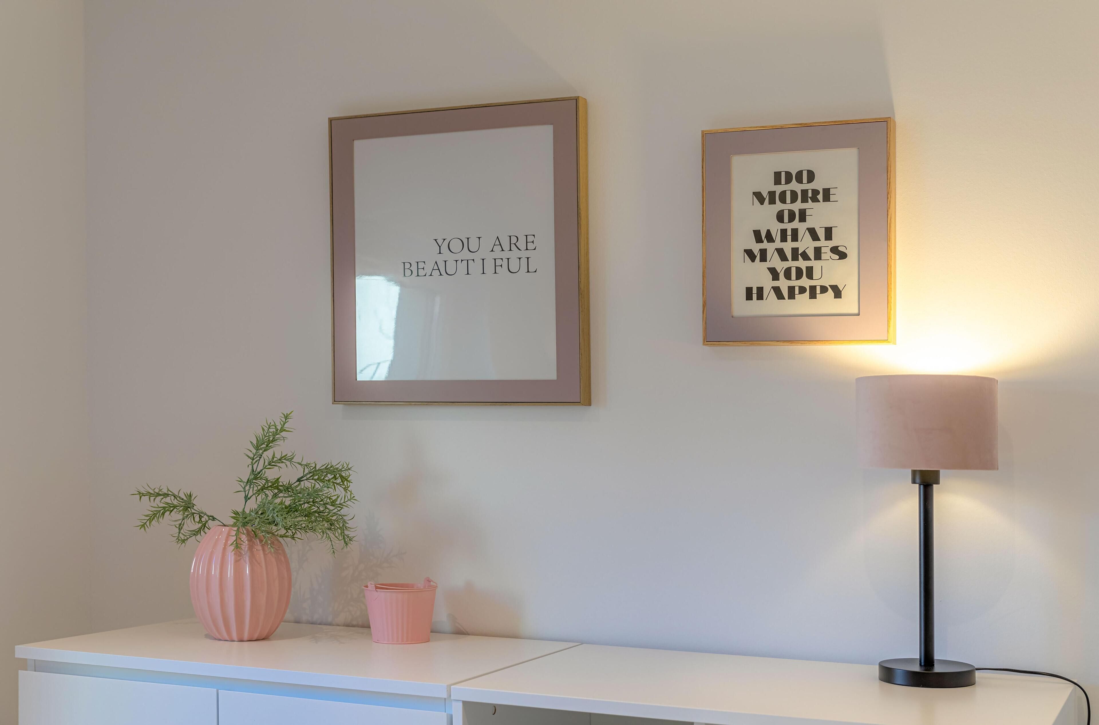 Pared con dos cuadros de citas motivacionales y un escritorio con una lámpara y una planta en maceta.