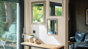 A modern interior with a glass door leading to an outdoor area, a wooden table with decorative vases, and a dark-colored sofa.
