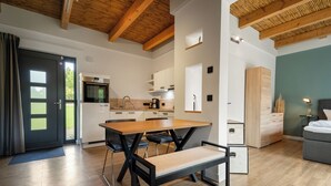 A modern kitchen with wooden beams, a dining area with a bench, and a living space with a sofa and a lamp.