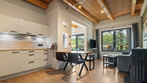 A modern kitchen with white cabinets, a wooden countertop, and a built-in stove. There is a dining area with a table and chairs, and a large window offering a view of the outdoors.