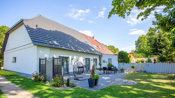 Uma casa moderna com telhado inclinado, um pátio com móveis de exterior e um jardim bem cuidado.