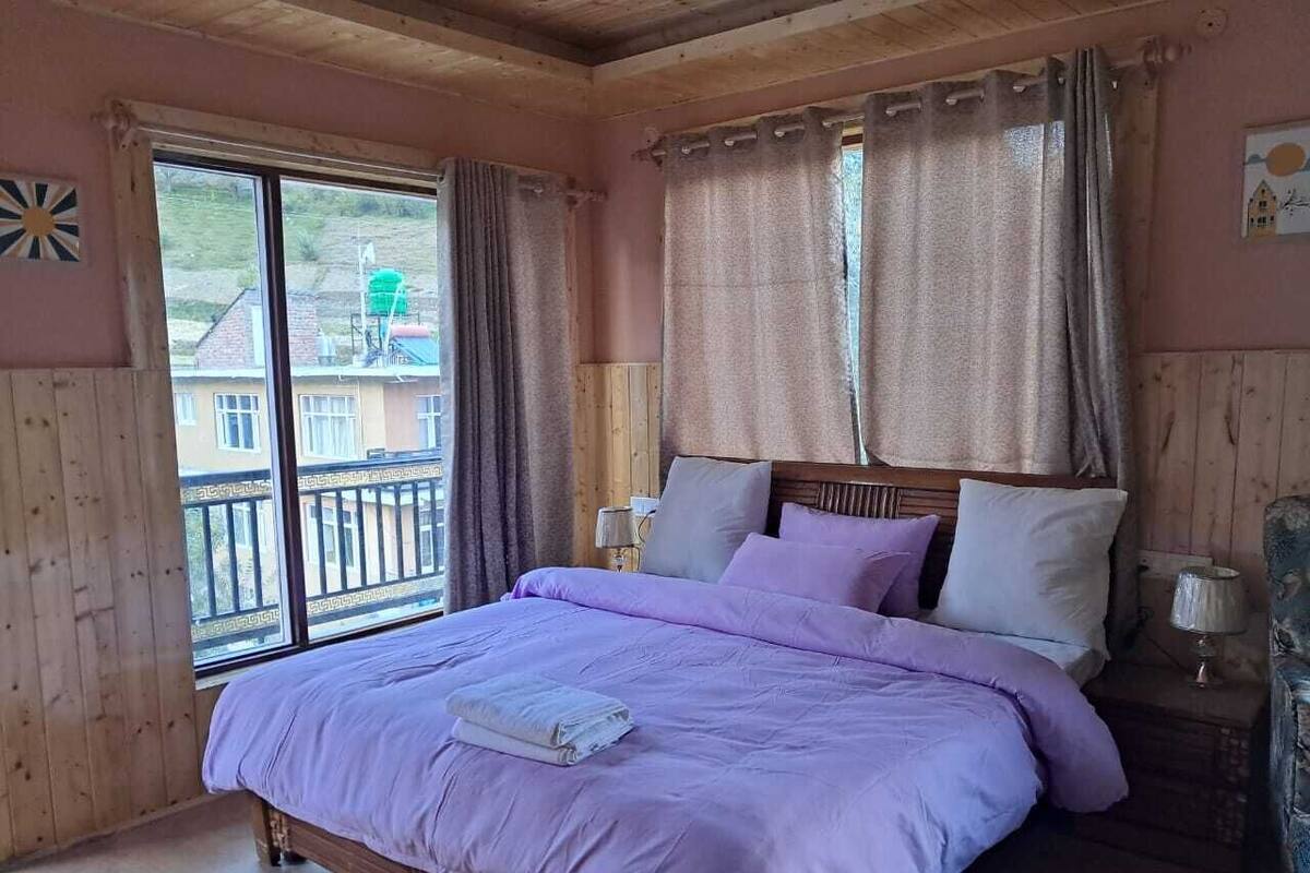 Quarto com cama grande, paredes de madeira, varanda e vista para prédios.