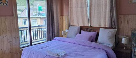A bedroom with a large bed, wooden walls, a balcony, and a view of buildings outside.