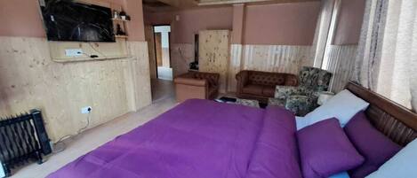 A bedroom with a large bed, a wooden ceiling, a TV mounted on the wall, and a wardrobe.