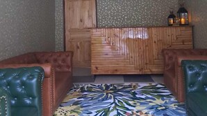 Ένα δωμάτιο με ένα διακοσμητικό χαλί, δύο δερμάτινες πολυθρόνες, ένα ξύλινο γραφείο υποδοχής και ένα πολυέλαιο.