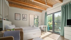 Ein modernes Hotelzimmer mit Holzbalkendecke, einem großen Bett, einem Schreibtisch und einem Balkon mit Blick auf Grünflächen.