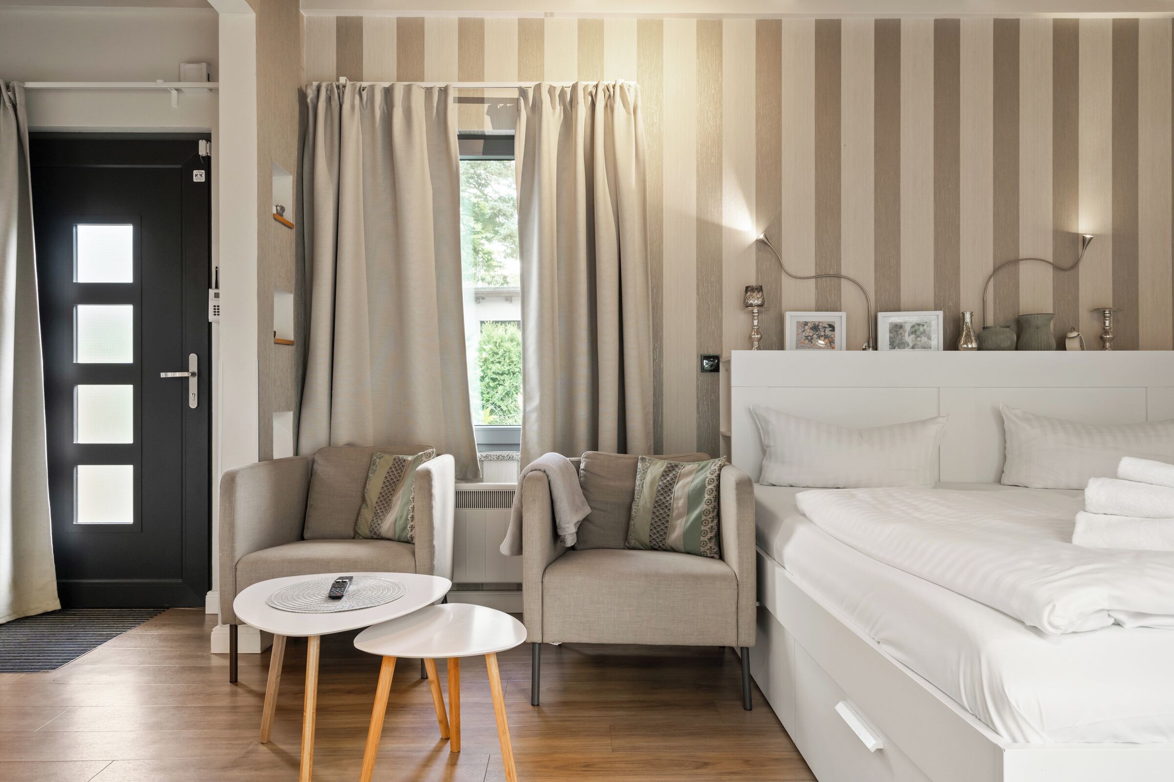 Een moderne slaapkamer met een bed, twee stoelen, een klein tafeltje en een raam met gordijnen.
