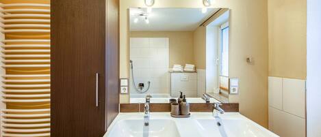 A bathroom with two sinks, a large mirror, and a shower.