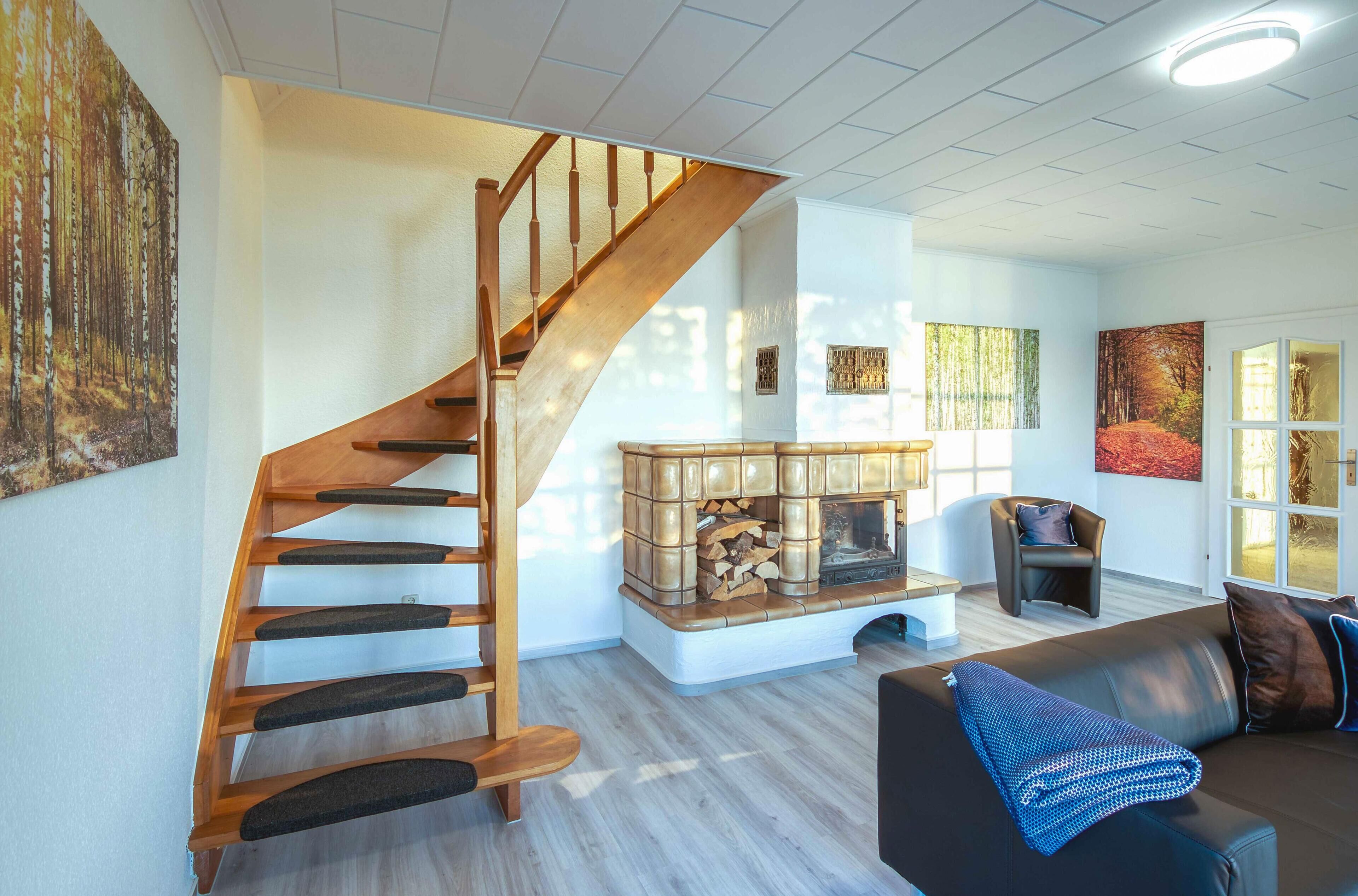 A staircase leading to a loft bedroom, a fireplace with a log fire, a black leather sofa, and a large window with a view.