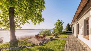 Una propiedad frente al lago con un patio, una mesa de comedor y un edificio con techo de paja.