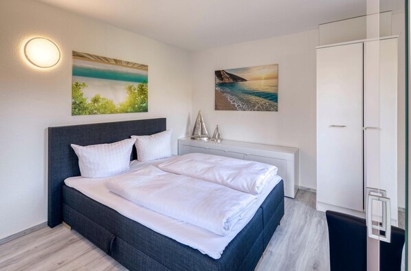 Un dormitorio moderno con una cama grande, una mesita de noche, un armario y dos cuadros colgados en la pared.