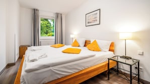 Una camera d'albergo con un letto, un comodino, una lampada, una finestra con tende e un quadro appeso al muro.