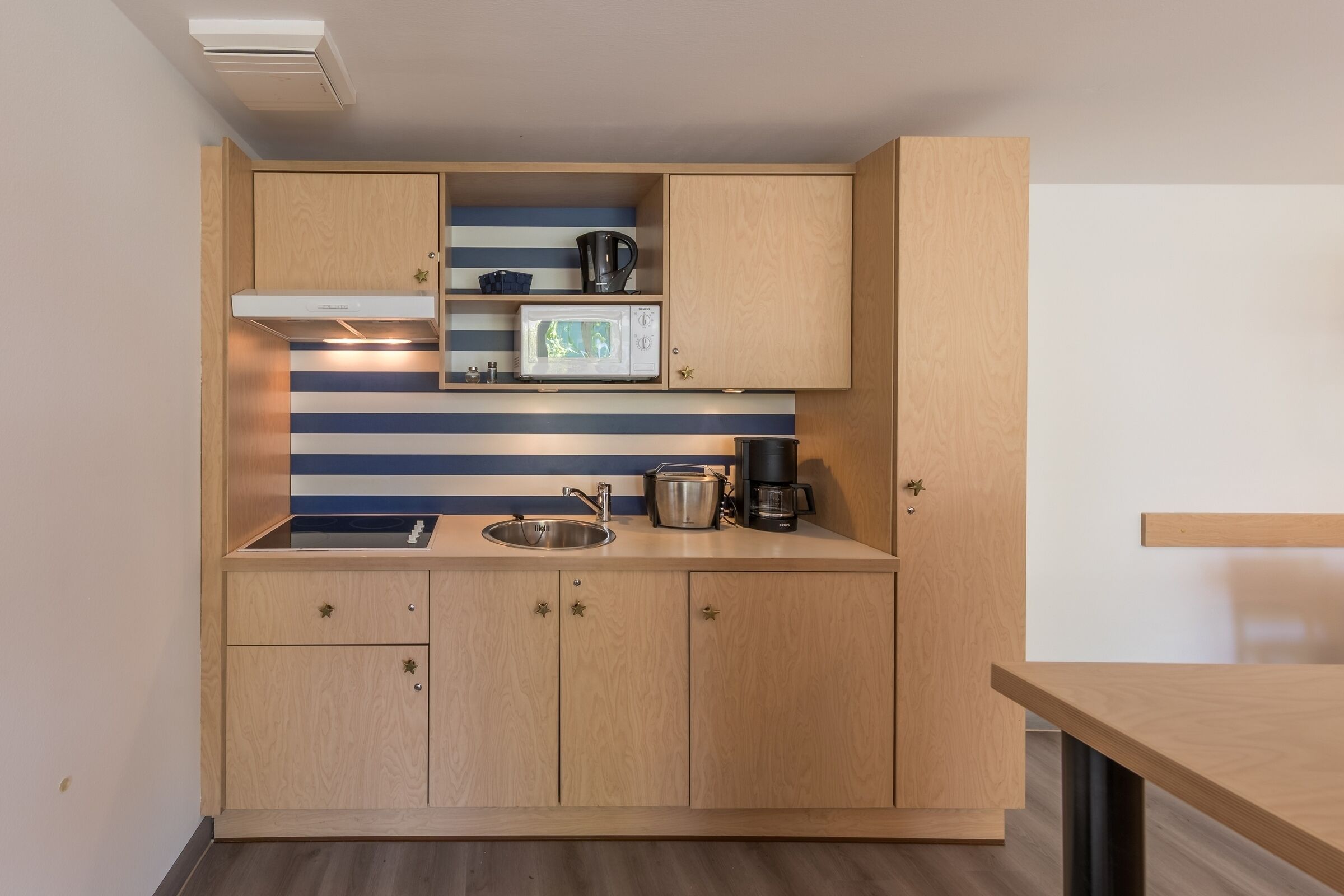 A compact kitchen with wooden cabinets, a microwave, a kettle, and a coffee maker.