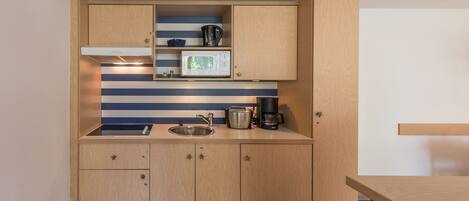 A compact kitchen with wooden cabinets, a microwave, a kettle, and a coffee maker.