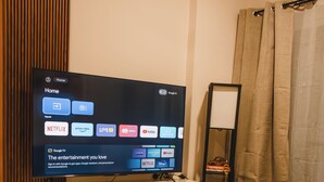 Una sala de estar moderna con una televisión de pantalla plana mostrando opciones de entretenimiento, una mesa de centro de madera, un sofá y un espejo.