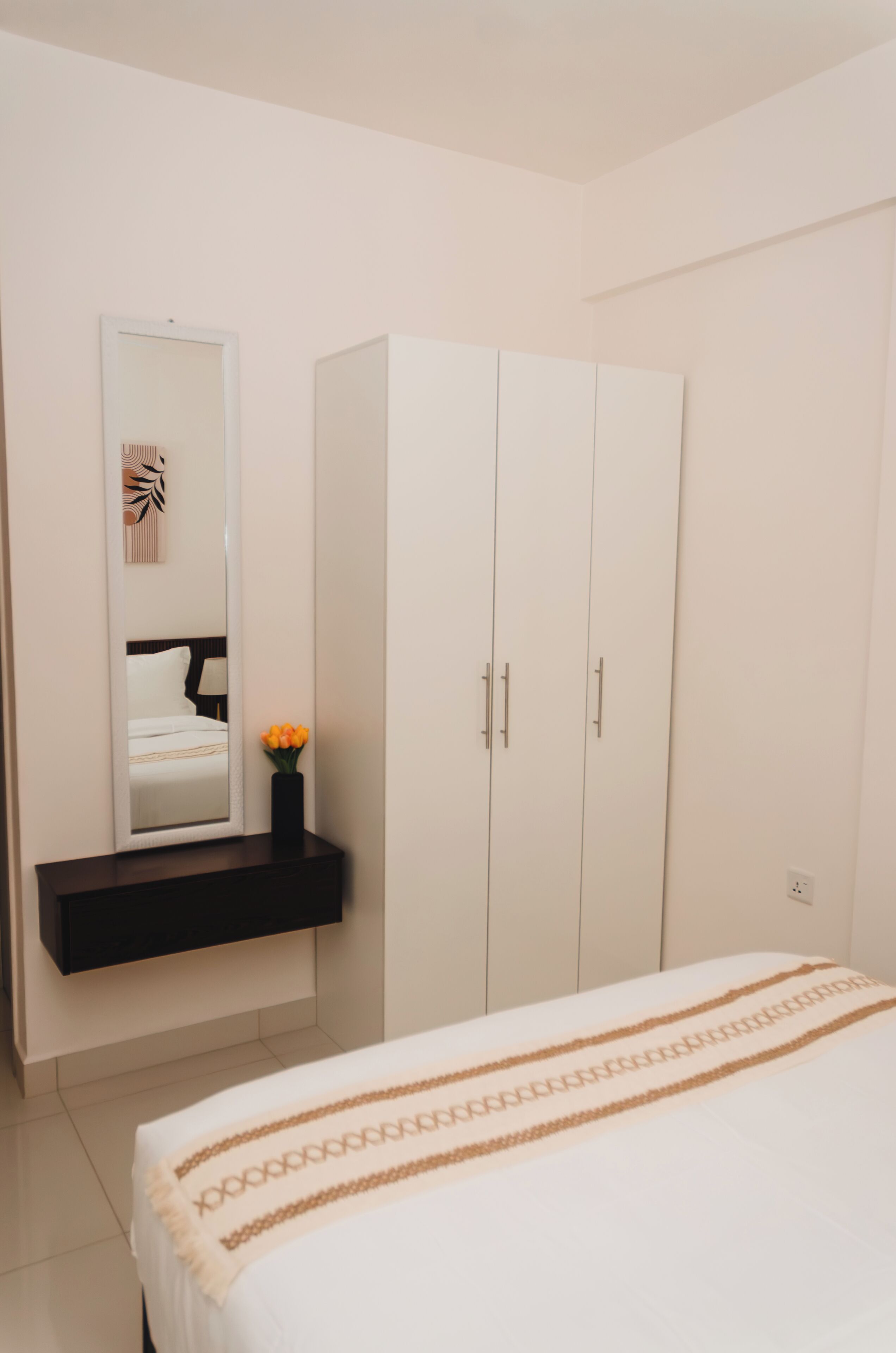 Een slaapkamer met een bed, een kledingkast, een spiegel en een klein tafeltje met een vaas.