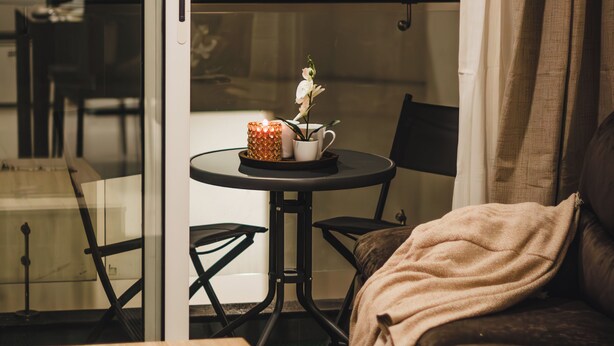 Una sala de estar acogedora con una mesa de centro de madera, un sofá y una pequeña mesa redonda con una vela y un florero.