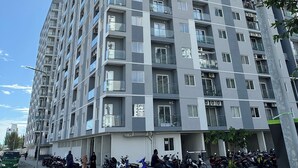 Un edificio residencial de gran altura con múltiples balcones, cielo despejado y motocicletas estacionadas en la planta baja.