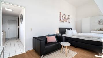 A modern bedroom with a black sofa, a bed, a bedside table, and a wall art piece.