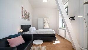 Et moderne soveværelse med seng, sort sofa, lille rundt bord og stort spejl.