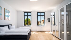 Ein modernes Schlafzimmer mit einem großen Bett, zwei Fenstern mit Aussicht, einem Kleiderschrank und einer Heizung.