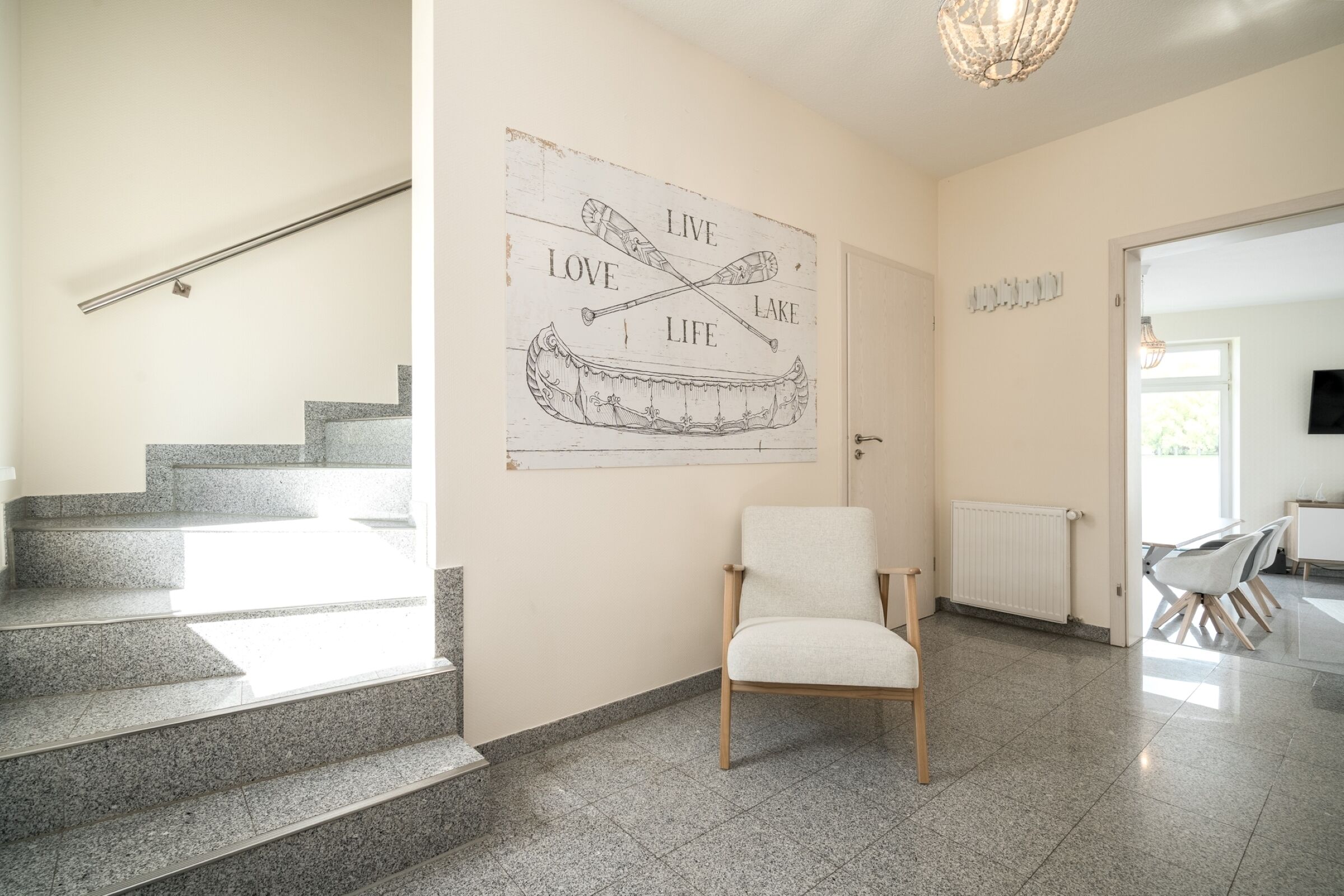 Een trap leidt naar een kamer met een kano en peddel kunstwerk, een witte stoel, en een eetgedeelte met stoelen.