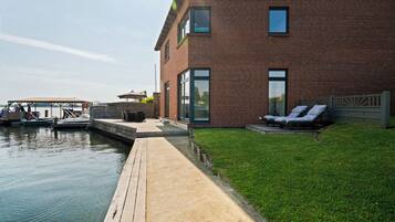 A waterfront property with a dock, a grassy lawn, and a brick building with large windows.