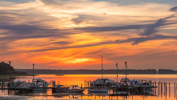 A marina with boats docked at wooden piers, surrounded by calm water and a sunset sky. - "Storchenflug" Vacation Apartment, Close to the Golf Course (Göhren-Lebbin)