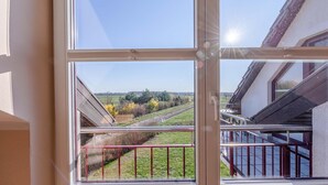 A window with a view of a rural landscape, including fields and trees. - "Storchenflug" Vacation Apartment, Close to the Golf Course (Göhren-Lebbin)
