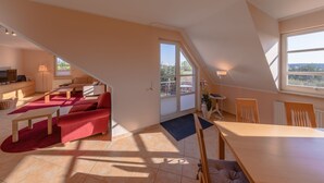 A spacious loft apartment with a high ceiling, a dining area, a living room with a red sofa, and a view through a large window. - "Storchenflug" Vacation Apartment, Close to the Golf Course (Göhren-Lebbin)
