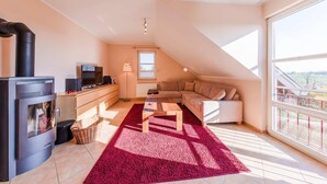 A modern living room with a fireplace, a sofa, a coffee table, and a large window. - "Storchenflug" Vacation Apartment, Close to the Golf Course (Göhren-Lebbin)