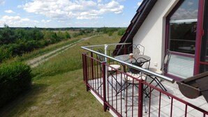 A balcony with a table and chairs, overlooking a rural landscape with fields and a path. - "Storchenflug" Vacation Apartment, Close to the Golf Course (Göhren-Lebbin)