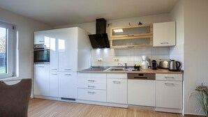 Una cucina moderna con mobili bianchi, forno integrato, piano cottura e macchina da caffè.
