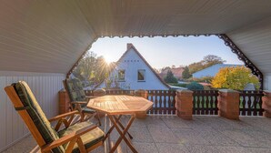 Patio esterno con tavolo e sedie in legno, muro in mattoni e vista su una casa e alberi.