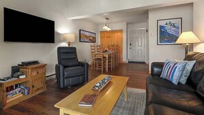Ein Wohnzimmer mit Flachbildfernseher, einem schwarzen Ledersofa, einem Holztisch und einem Essbereich mit Holztisch und Stühlen.