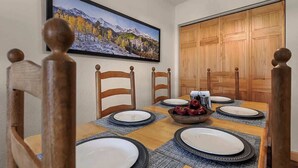 Ein Essbereich mit einem Holztisch, gedeckt für vier Personen, einem gerahmten Landschaftsbild darüber und einer Holztür rechts.