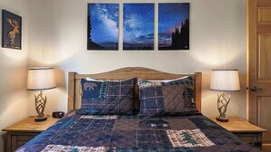 Ein Schlafzimmer mit einem Holz-Kopfteil, einer gesteppten Bettdecke, zwei Nachttischlampen und drei Bildern vom Sternenhimmel an der Wand.