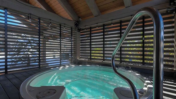 Ein Whirlpool mit Holzboden und Metallgeländern, umgeben von Fenstern mit Jalousien.