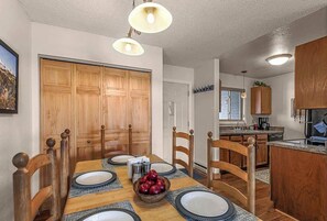 Enjoy meals in this dining area with a table for four, a bowl of fresh fruit, and a kitchen nearby.
