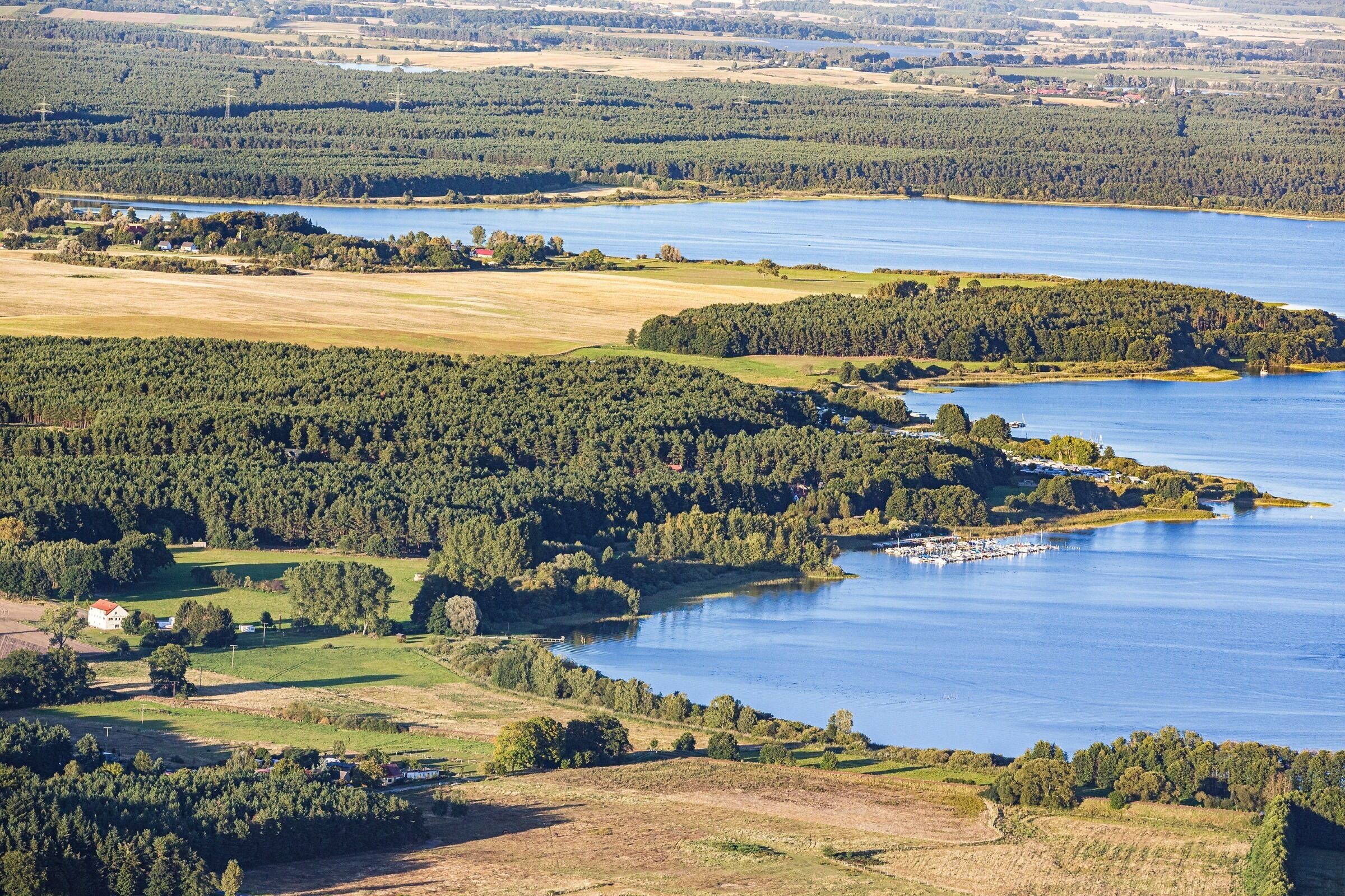 Une vue aérienne d’un lac entouré de zones boisées et de champs.