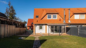 Une maison à deux étages, avec un toit en tuiles, une terrasse couverte et un jardin clôturé.