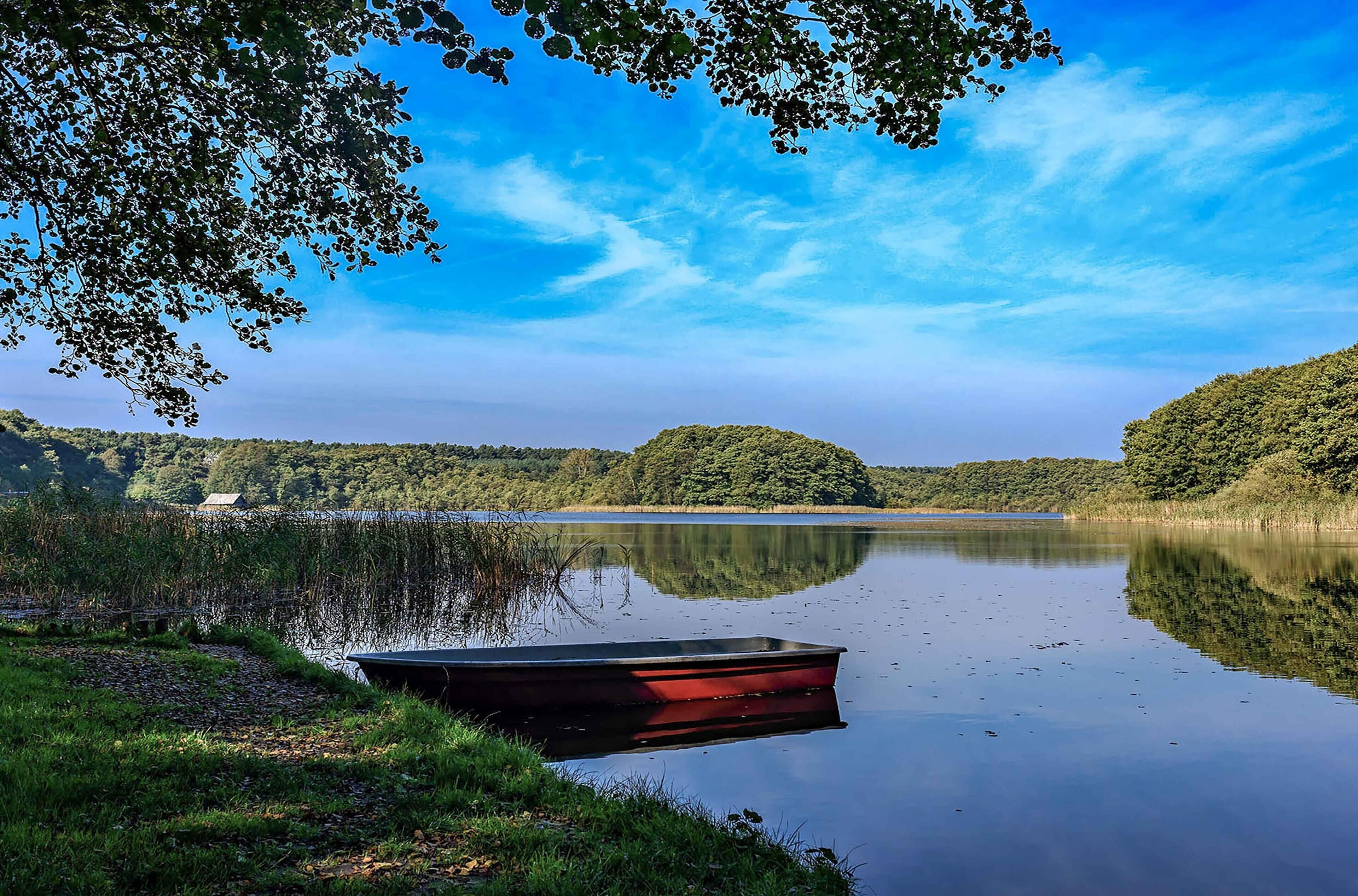 A calm lake with a small boat docked on the shore, surrounded by lush greenery and hills.