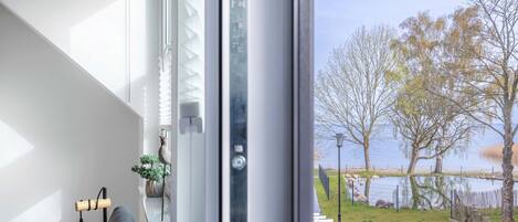 A modern room with a large window, a hanging light fixture, and a view of a lake with a wooden deck.
