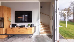 Un salon moderne doté d’un grand téléviseur à écran plat, de meubles en bois et d’un escalier menant à un espace extérieur.