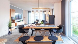 Un espace repas moderne avec une table en bois, des chaises noires et un banc. Une grande fenêtre offre une vue sur l’extérieur.