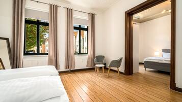 Ein Hotelzimmer mit Holzboden, einem Bett, einem Stuhl und Blick auf die Straße durch große Fenster.
