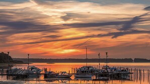 Una marina con barcos amarrados a muelles de madera, rodeada de agua tranquila y un cielo al atardecer.